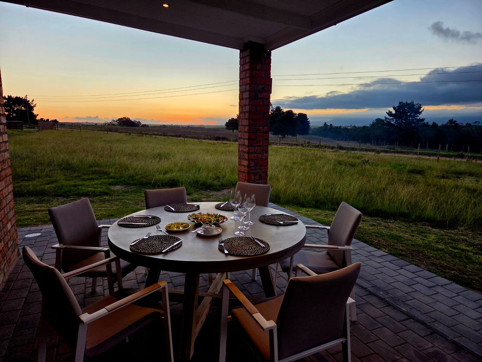 Stoep dining table set at Plaasrus — sunset over the pasture, Outeniqua range behind